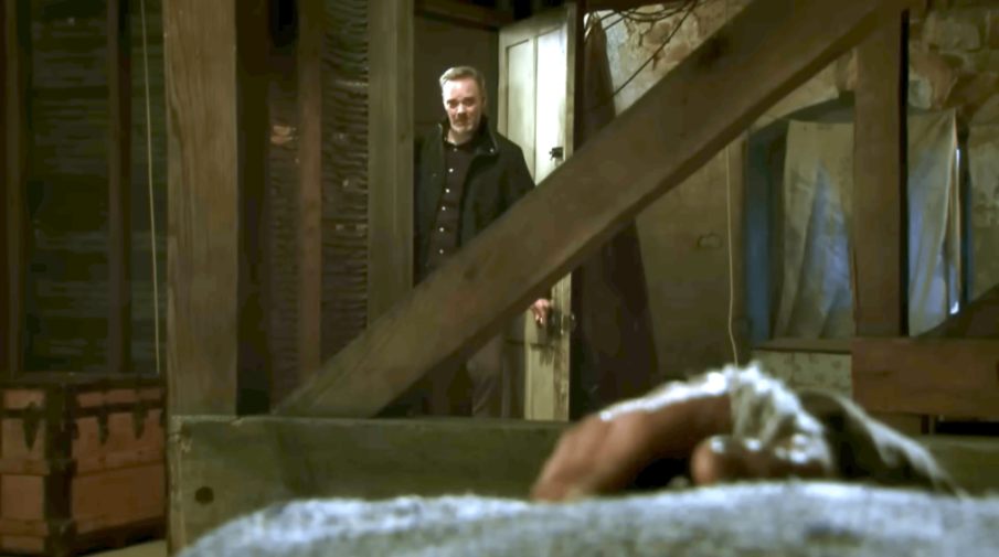 A man stands in a doorway, looking down at someone on the floor.