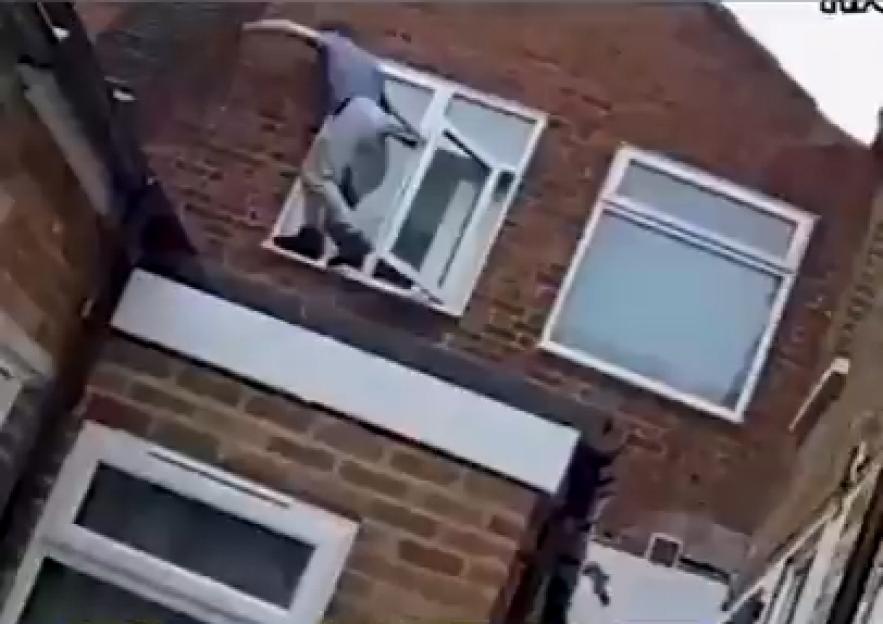 A person climbing through a broken window on a brick building.