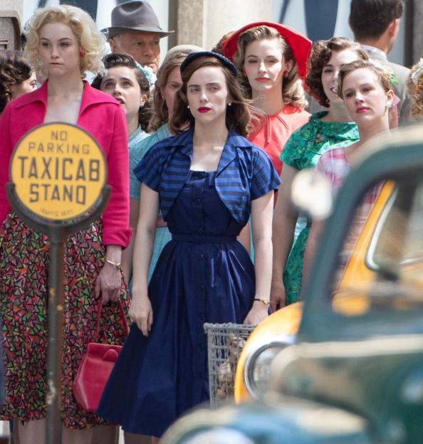 Billie Eilish on set for The Bell Jar adaptation, wearing a blue dress and surrounded by other actors in period attire.
