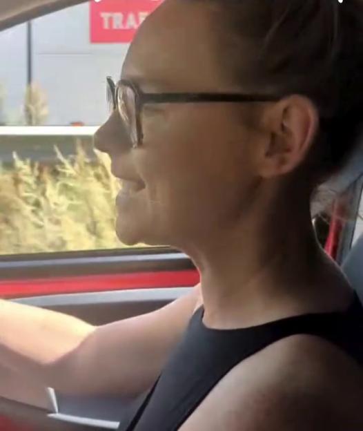 Natalie Ann Jamieson driving a car, wearing glasses and a black top, with text overlay.