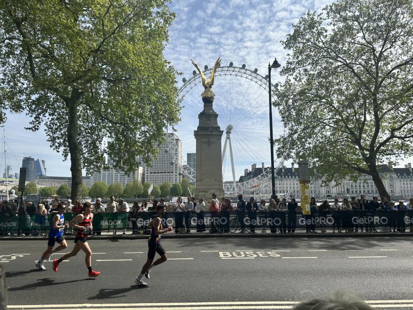 Runners in the London Marathon with the London Eye and a golden statue in the background.