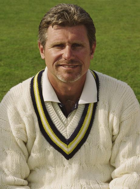 Robin Smith, a male cricketer, wearing a white, V-neck, cable-knit cricket sweater with yellow and black striped trim.