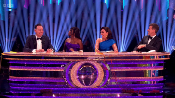 Strictly Come Dancing judges Motsi Mabuse, Craig Revel Horwood, Shirley Ballas, and Anton Du Beke at a glittery purple judging desk.
