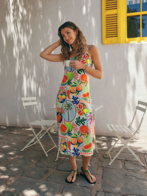 Woman in a fruit-patterned holiday dress holding a cup.