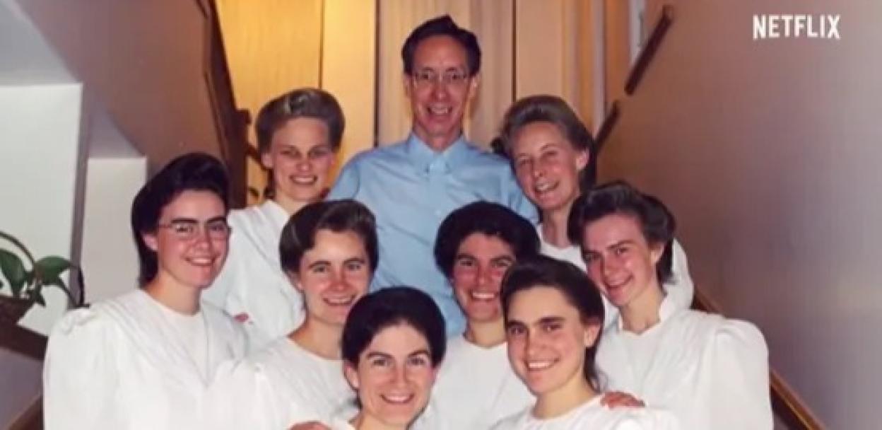 Warren Jeffs posing with seven women in white dresses.