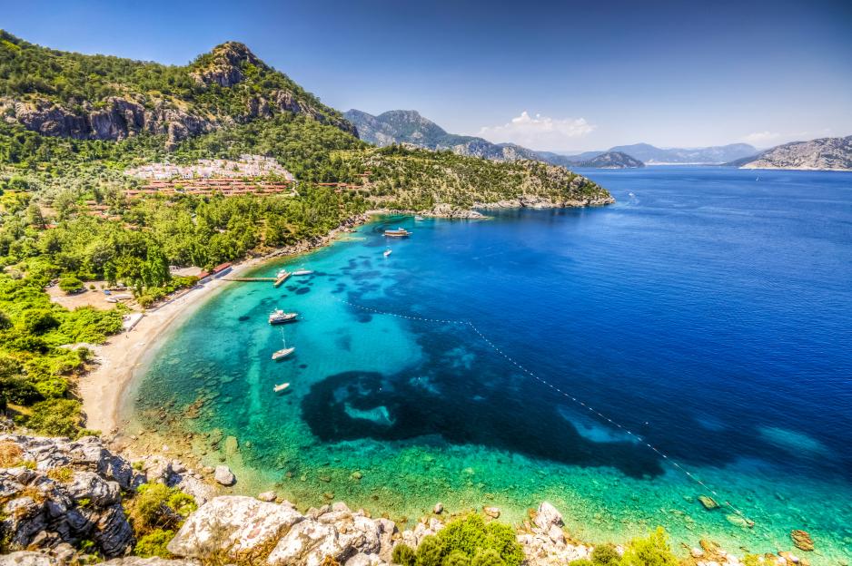 View of Turunc Bay in Marmaris, Turkey, with boats in the turquoise water and a town at the base of a green mountain.