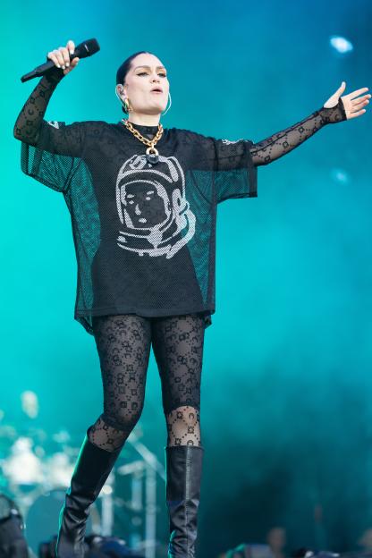 Jessie J performing on stage, wearing a black mesh top with a white astronaut graphic and black patterned leggings.