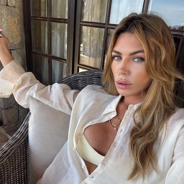 Abbey Clancy looking at the camera, wearing an unbuttoned white shirt revealing a cream top and two necklaces.