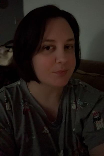 A woman with short dark hair and a nose piercing looks at the camera.