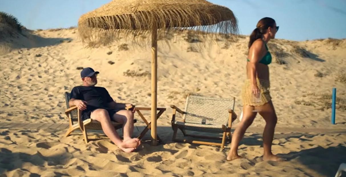 Wayne and Coleen Rooney on a sandy beach under a straw umbrella.